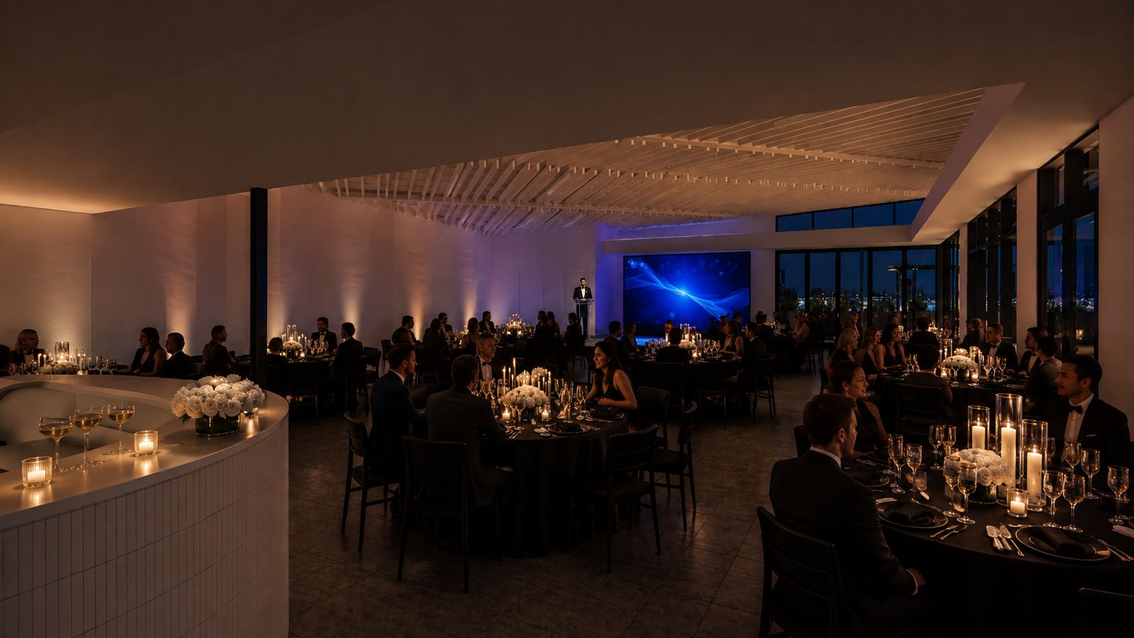 Indoor reception with a stage and screen, violet and blue uplighting washing the room.